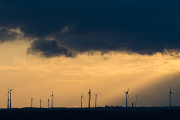 Fototapeta na wymiar Windräder auf einem Feld im dramatischen Sonnenaufgang