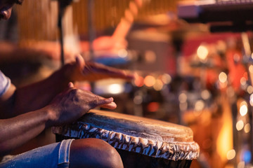 Close-up of man's hands playing on African djembe drum, selective focus on hands with blurry...