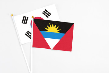 Obraz premium Antigua and Barbuda and South Korea stick flags on white background. High quality fabric, miniature national flag. Peaceful global concept.White floor for copy space.