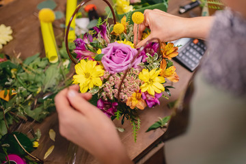 Florist woman makes bouquet flowers of pink roses, yellow chrysanthemums in gift box. Top view on workplace. Concept considers value business calculator