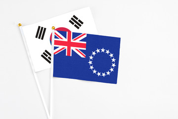 Fototapeta premium Cook Islands and South Korea stick flags on white background. High quality fabric, miniature national flag. Peaceful global concept.White floor for copy space.