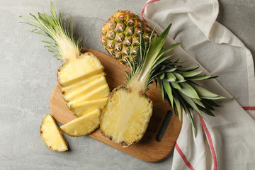 Cutting board with pineapples on grey background, top view