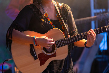 close-up view of musician woman playing guitar on the stage, female guitarist hands during night...