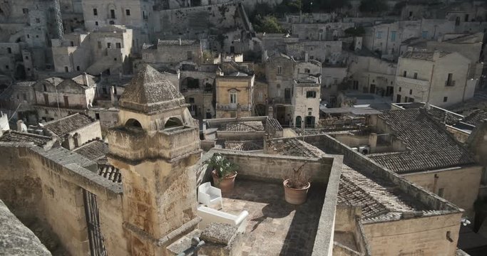 Roofs of houses in the Sassi of Matera transformed into hotels. Panoramic terrace with sofa and chair in white plastic.