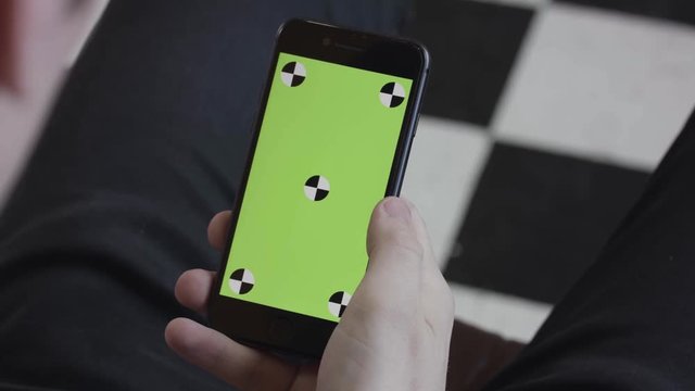 Man hands using mobile smartphone with green screen, over the shoulder view. Stock footage. Close up of man scrolling and tapping on Iphone screen with chroma key.