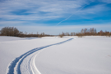 Fototapeta na wymiar Snowmobile trail on a snowy field. Forest in the background.