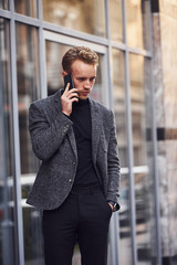 Man in elegant formal wear outside against modern building talking by the phone