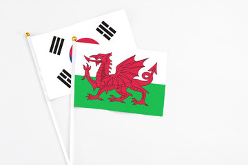 Wales and South Korea stick flags on white background. High quality fabric, miniature national flag. Peaceful global concept.White floor for copy space.
