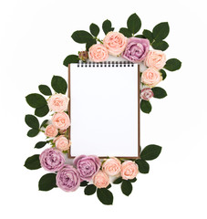 Leaf notebook in a frame of pink roses flowers and green leaves. Isolated on white background. View from above. View top. Flat lay.