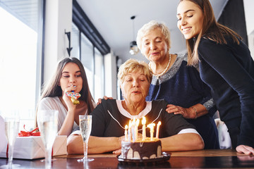 Blowing the candles. Senior woman with family and friends celebrating a birthday indoors