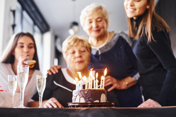 Blowing the candles. Senior woman with family and friends celebrating a birthday indoors
