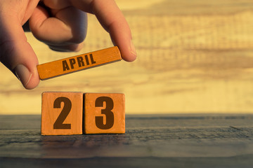 april 23rd. Day 23 of month,calendar on a wooden cube. a woman's hand puts the name of the month on the number of the month on a wooden background spring, day of the year concept