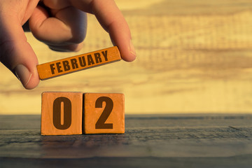 february 2nd. Day 2 of month,calendar on a wooden cube. a woman's hand puts the name of the month on the number of the month on a wooden background winter, day of the year concept