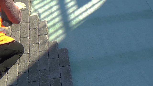 Construction worker laying interlocking paving concrete onto sheet nonwoven bedding sand and fitting them into place.