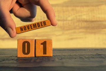 november 1st. Day 1 of month, calendar on a wooden cube. a woman's hand puts the name of the month on the number of the month on a wooden background autumn, day of the year concept