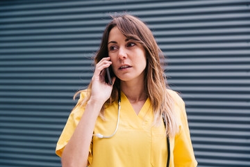 Chica joven manteniendo conversación telefónica desde su smartphone durante su descanso en el trabajo de enfermera.