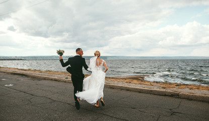 Young wedding beautiful couple, newlyweds running along the beach in honeymoon or wedding day after ceremony