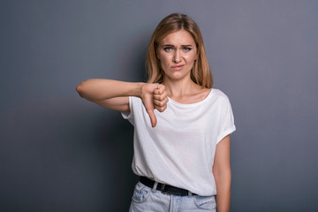 Fototapeta premium Caucasian woman in neutral casual outfit standing on a neutral grey background. Portrait with emotions: angry, pain, sickness and despair