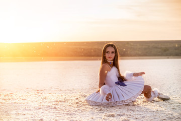 Tender young ballerina dancer in a snow-white tutu dress and white pointe shoes on a salty dried...