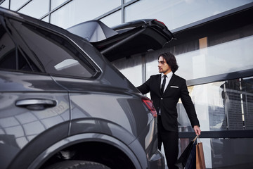 Fototapeta na wymiar Portrait of handsome young businessman in black suit and tie outdoors near modern car