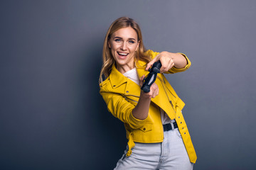 Caucasian woman in neutral casual outfit standing on a neutral grey background. She playing game using joystick with VR goggles and smiling happily