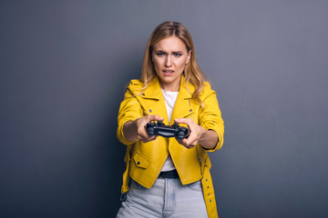 Caucasian woman in neutral casual outfit standing on a neutral grey background. She playing game using joystick with VR goggles and smiling happily