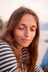 Portrait of a beautiful red-haired girl in T-shirt near the sea at the sunset. Pensive and happy girl. Relaxing near ocean. pretty girl