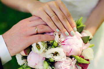 Obraz na płótnie Canvas Hands of newlyweds on the background of wedding bouquet. Gold wedding rings on the finger of bride and groom, close-up. Concept of a wedding celebration.