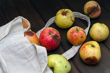 Zero waste concept. Red and yellow ugly apples in white textile bag on wooden background.