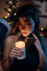 Beautiful woman holding a burning candle in her hands. Waiting for the New Year holidays. Christmas candle. Christmas decor.