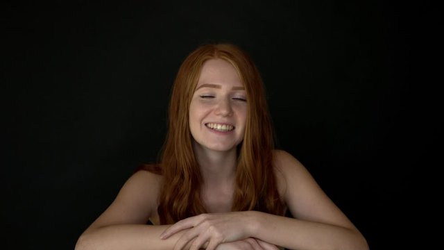 Close up of happy giggling ginger hair girl on isolated black background as she smiles on front of the camera ideal for happiness feminine campaign