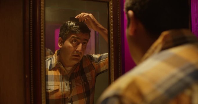 An insecure middle-aged man, combing his hair in front of the mirror, searching for the courage for an important announcement. Handheld shot.