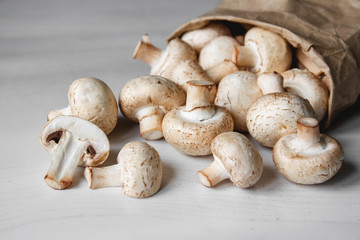 Mushrooms champignons in paper bag on a white wooden table. Place for text or advertising. Top view
