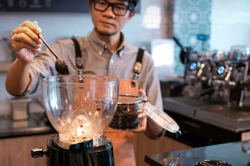 Asian barista scoop the coffee beans to grind in the coffee grinder, start-up business concept
