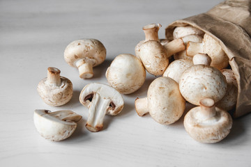 Mushrooms champignons in paper bag on a white wooden table. Place for text or advertising. Top view