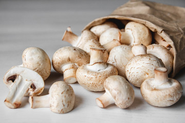 Mushrooms champignons in paper bag on a white wooden table. Place for text or advertising. Top view
