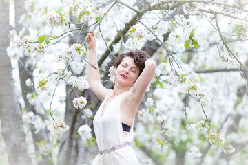  A portrait of beautiful young Caucasian woman with curly dark hair in blossoming orchard