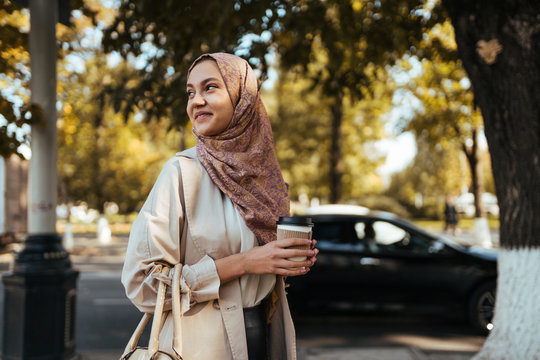muslim woman on the street with coffee in hand, turned over her shoulder and smiles on the street