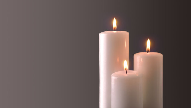 Three burning candles on gray degrading background