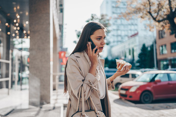 Fototapeta premium girl anxiously speaks on the phone and holds in her hand a hamburger on the street
