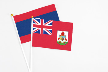 Fototapeta premium Bermuda and Laos stick flags on white background. High quality fabric, miniature national flag. Peaceful global concept.White floor for copy space.