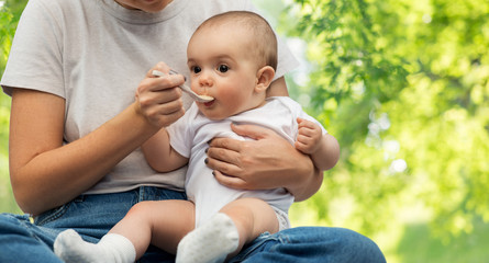 child, eating and food concept - close up of mother with spoon feeding little baby over green natural background