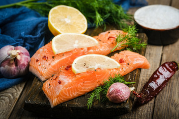 Fresh salmon steaks with herbs, lemon, rosemary and spices on a cutting board on a rustic...