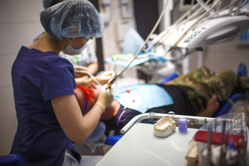 Dentist in overalls, face mask, cap and rubber gloves in the process. Female dentist treats the patient in the dental chair.