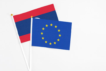 European Union and Laos stick flags on white background. High quality fabric, miniature national flag. Peaceful global concept.White floor for copy space.