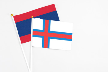 Obraz premium Faroe Islands and Laos stick flags on white background. High quality fabric, miniature national flag. Peaceful global concept.White floor for copy space.