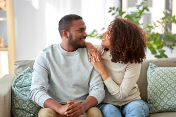 relationships and people concept - happy african american couple sitting on sofa at home