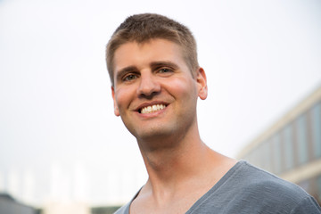 Content young man smiling at camera. Portrait of cheerful young man in grey t-shirt standing on street and smiling at camera. Emotion concept