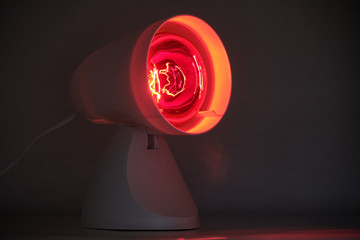 Infrared lamp glowing in the dark with its warming red light to cure for example colds or tensions.