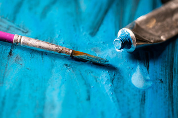 Blue paint tubes with paintbrushes on the painted canvas background. Creative colored wallpaper....